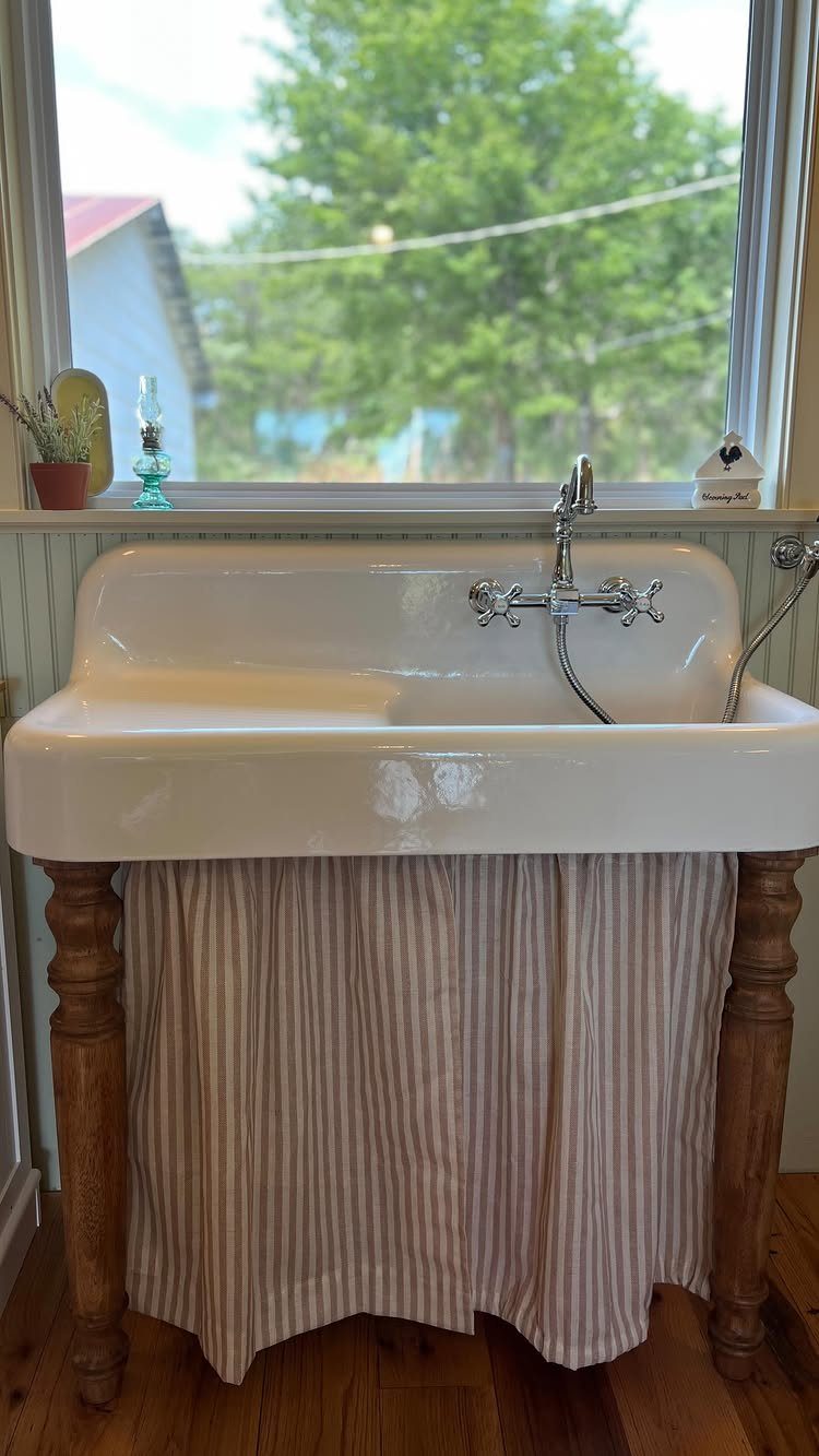 White ceramic farmhouse sink with wooden legs and a striped fabric curtain under the basin.