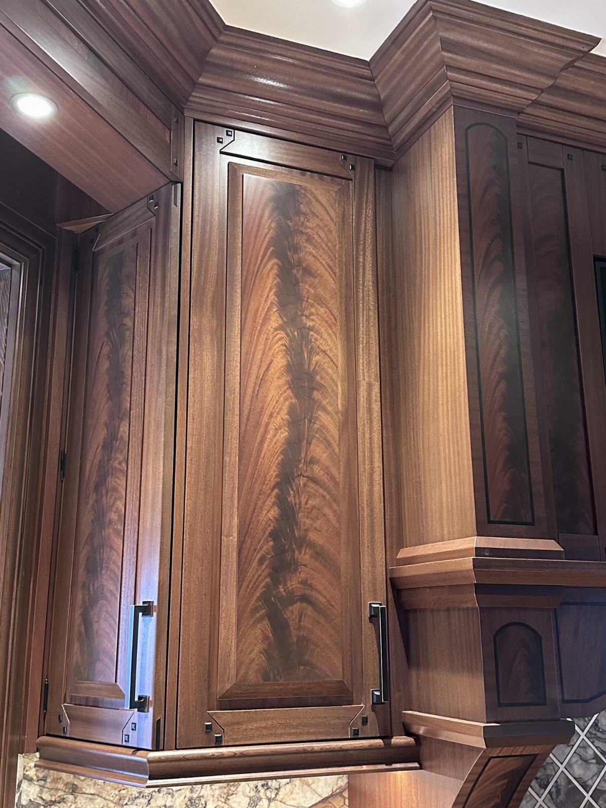 Ornate dark reddish-brown wood kitchen cabinets with decorative molding and black metal handles.