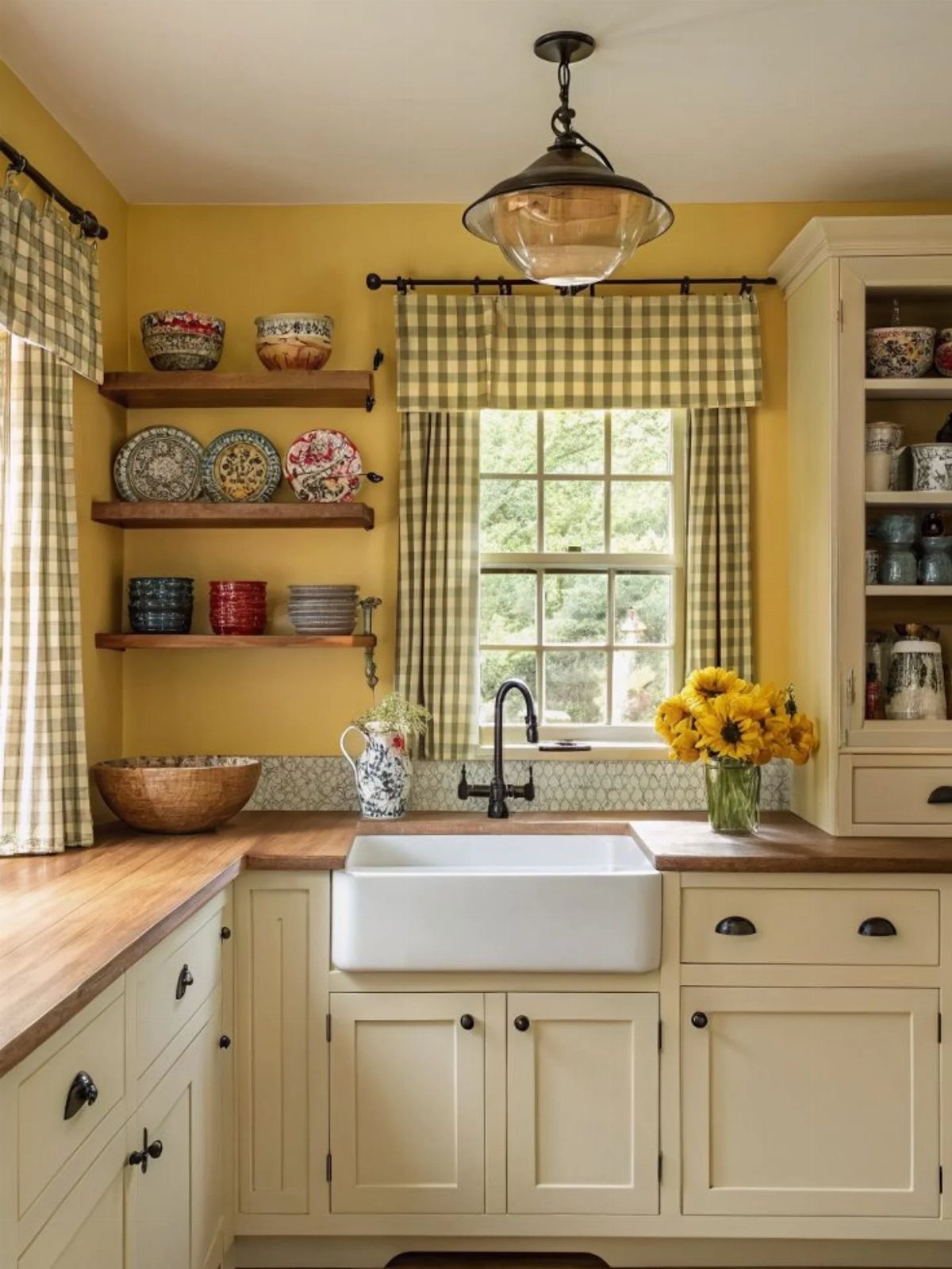 Bright yellow kitchen walls with cream cabinets, farmhouse sink, and checkered curtains.