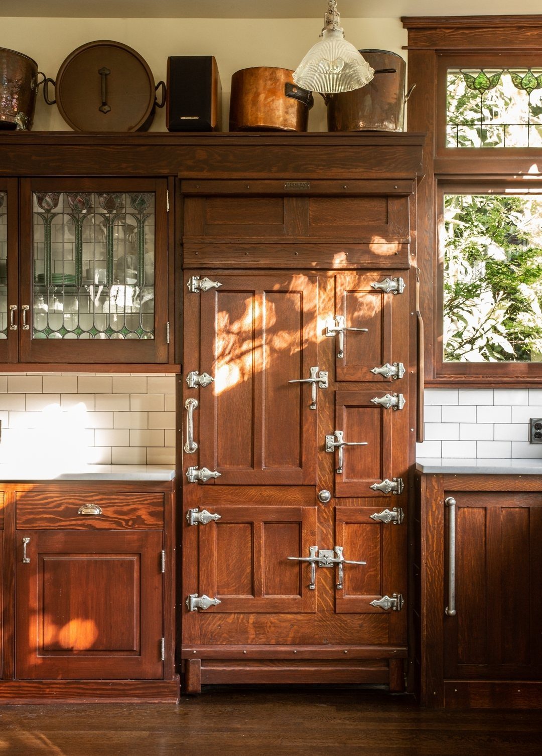 Vintage wooden icebox with silver latches built into dark wood kitchen cabinetry.