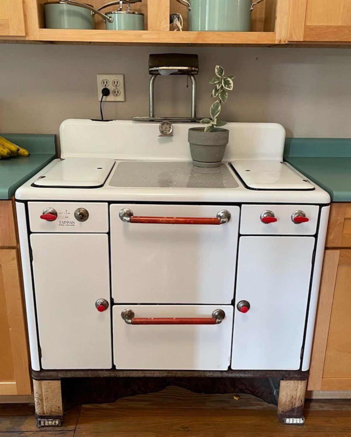 Vintage white porcelain enamel stove with red handles in a kitchen with teal counters.