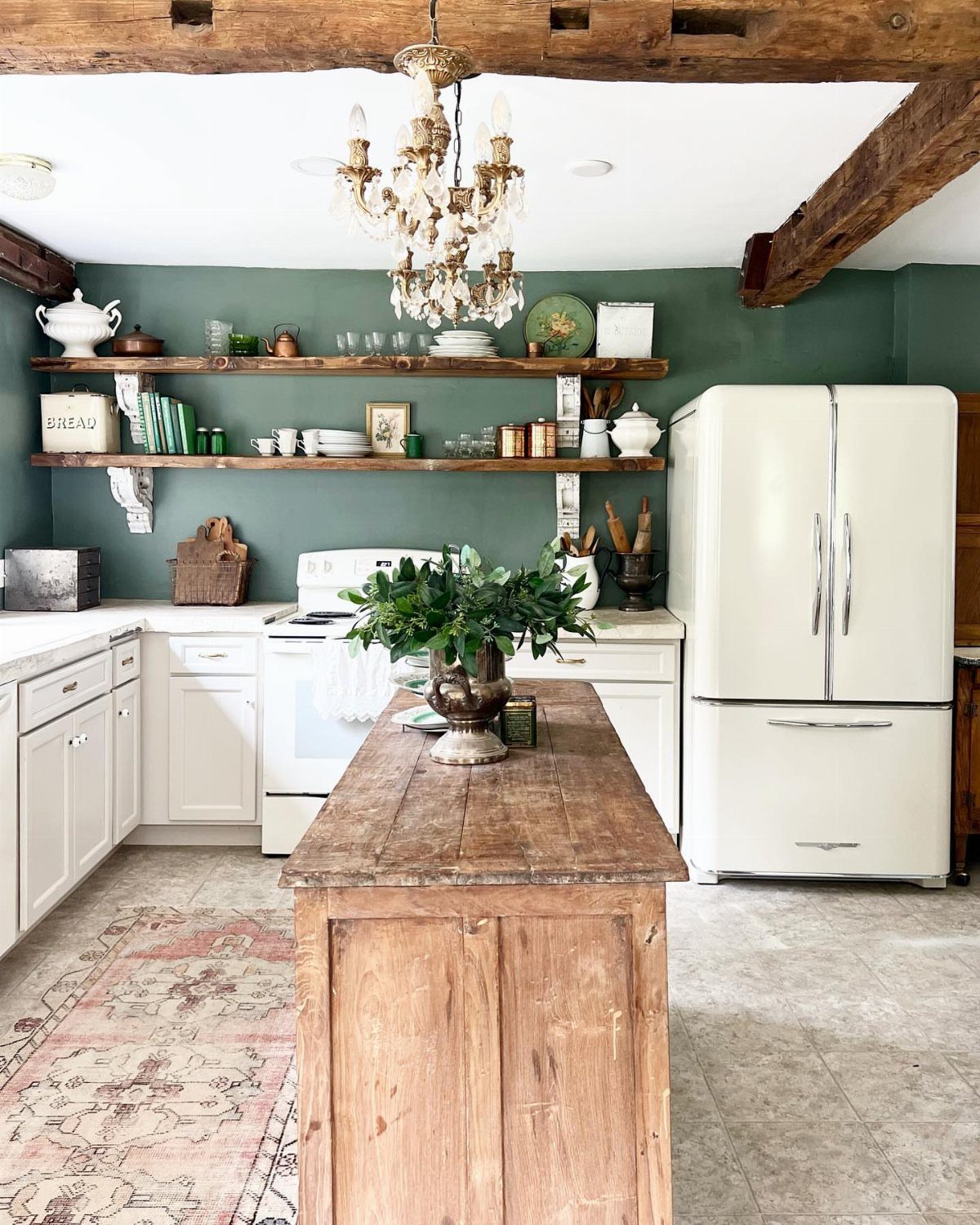 Rustic kitchen with sage green walls, wooden island, and vintage white refrigerator.
