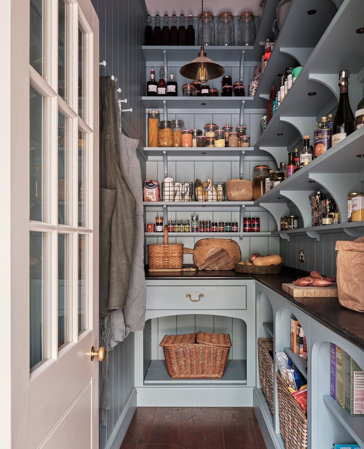 Walk-in pantry with light blue shelving, glass jars, and woven baskets.
