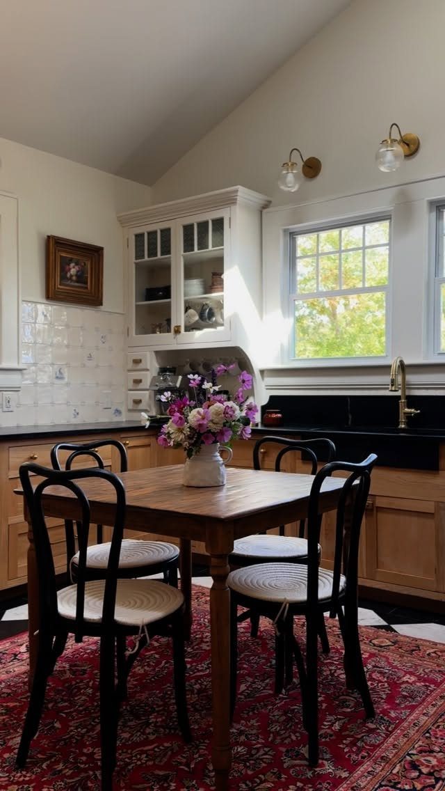 Rustic kitchen with wooden table, black bentwood chairs, and red patterned rug.
