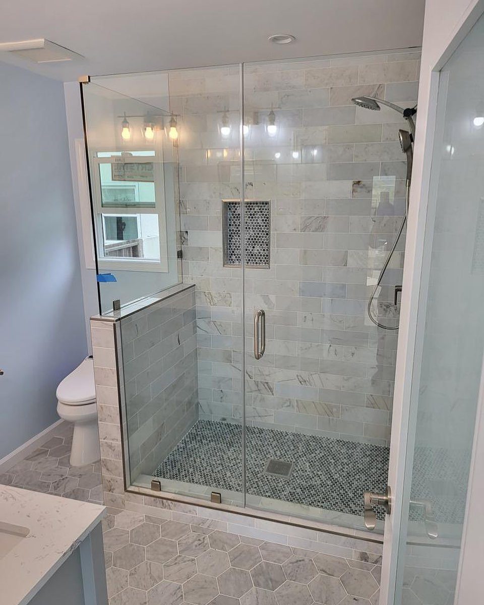Corner walk-in shower with frameless glass doors and white marble wall tiles.