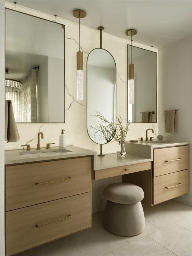 Modern bathroom vanity with gold pendant lighting and three mirrors on marble walls.