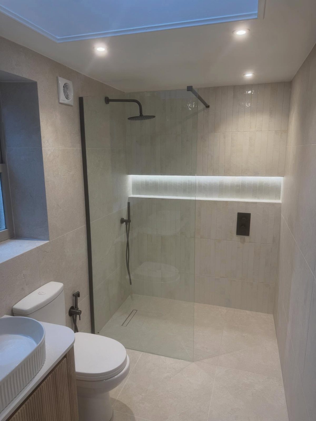 Walk-in linear shower with frameless glass and recessed lighting in a beige bathroom.