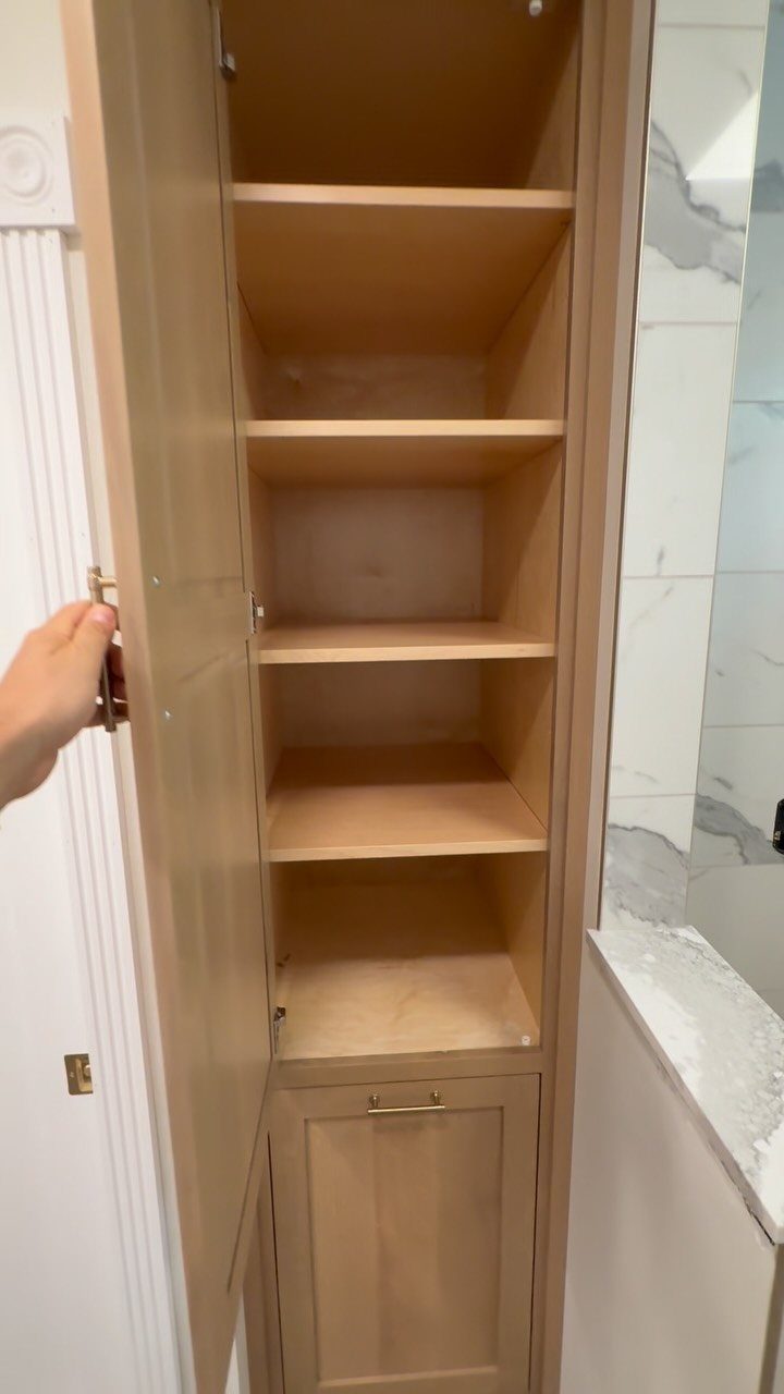 Light wood linen closet with open shelves and a bottom cabinet in a bathroom.