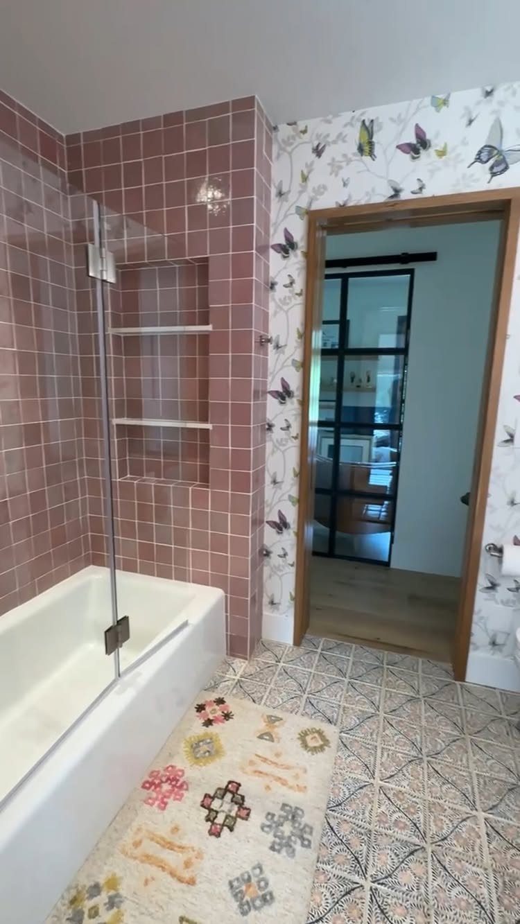 White bathtub with glass shower partition and pink tiled walls in a bathroom.