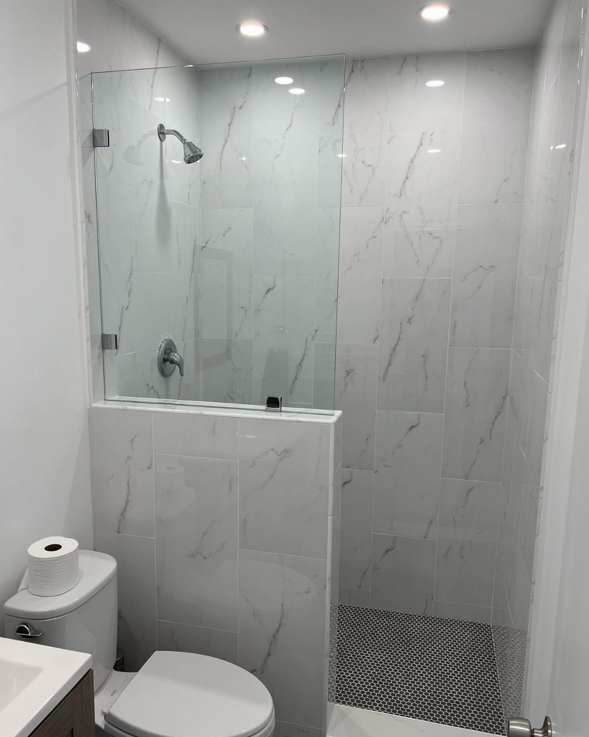 Walk-in shower with white marble tiles and a frameless glass partition in a bathroom.