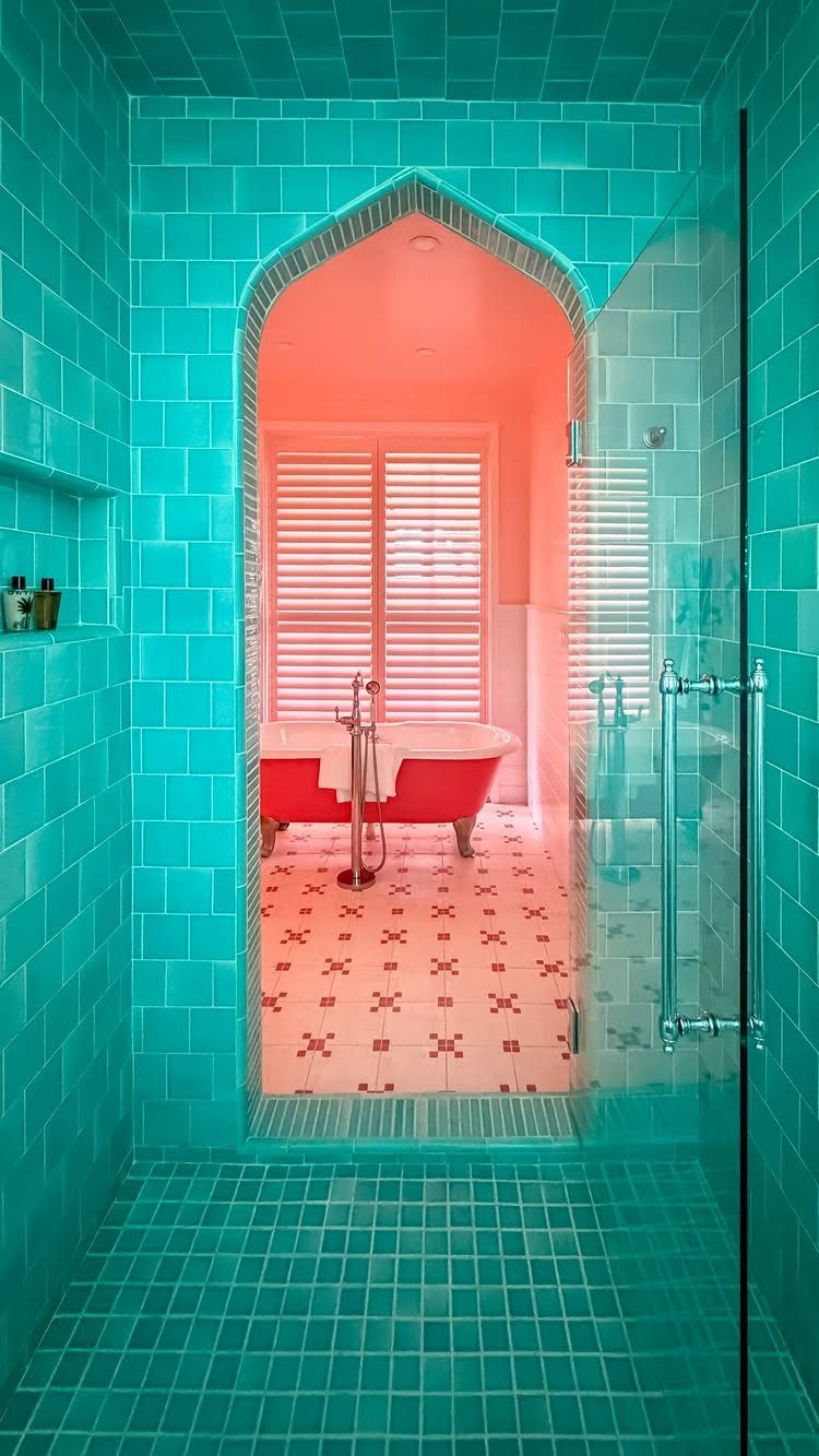 Turquoise tiled walk-in shower looking through an archway toward a red clawfoot bathtub.