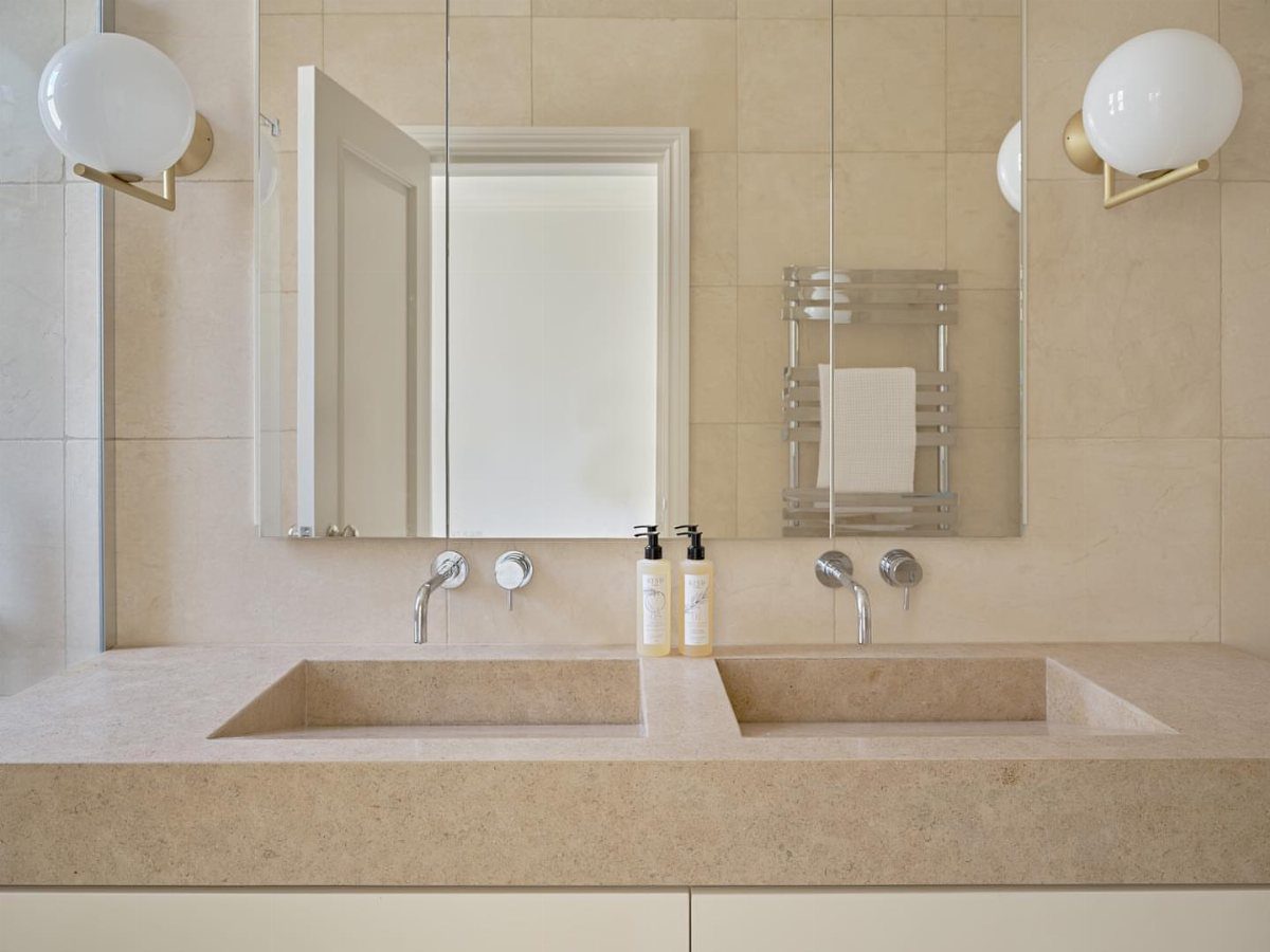Beige integrated stone double sink and countertop in a modern bathroom with mirrors.