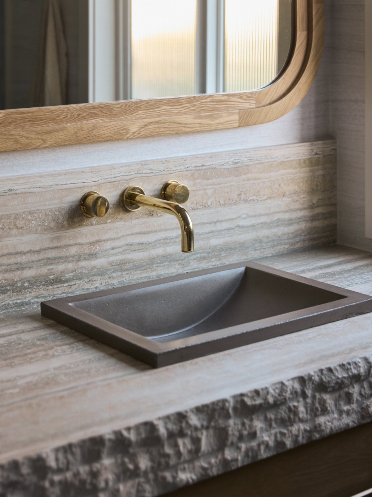 Dark grey rectangular drop-in basin in a textured stone countertop with gold faucet.