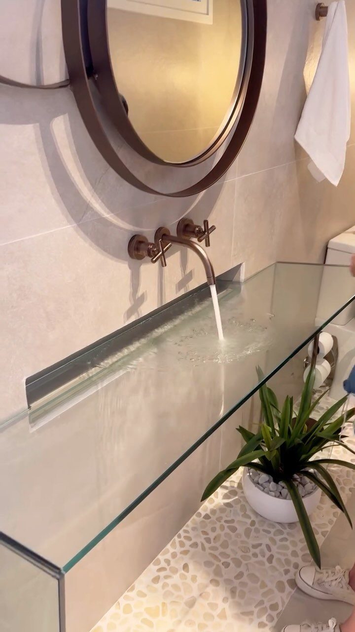 Glass countertop with integrated sink and wall-mounted bronze faucet in a modern bathroom.