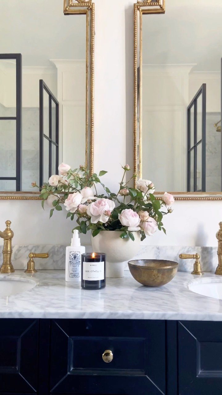 Navy blue bathroom vanity with white marble countertop and gold faucets and mirrors.
