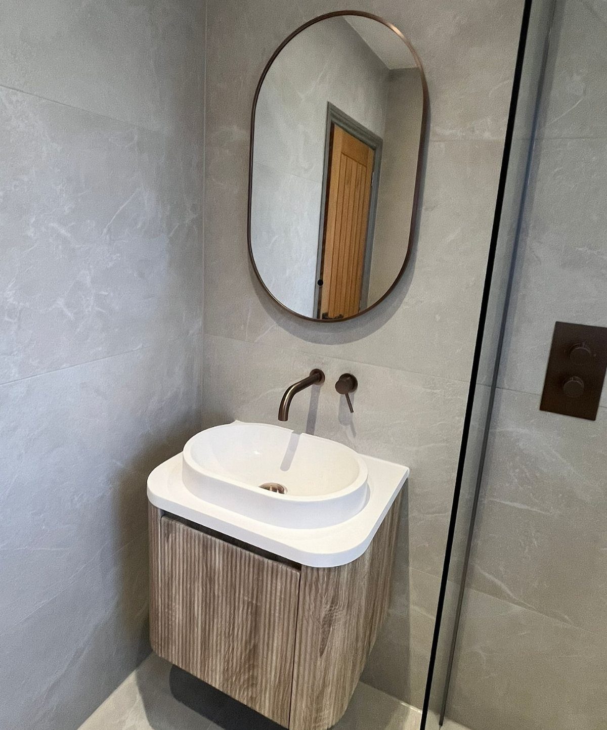 White oval vessel sink on a wood-grain vanity with a matching oval mirror.