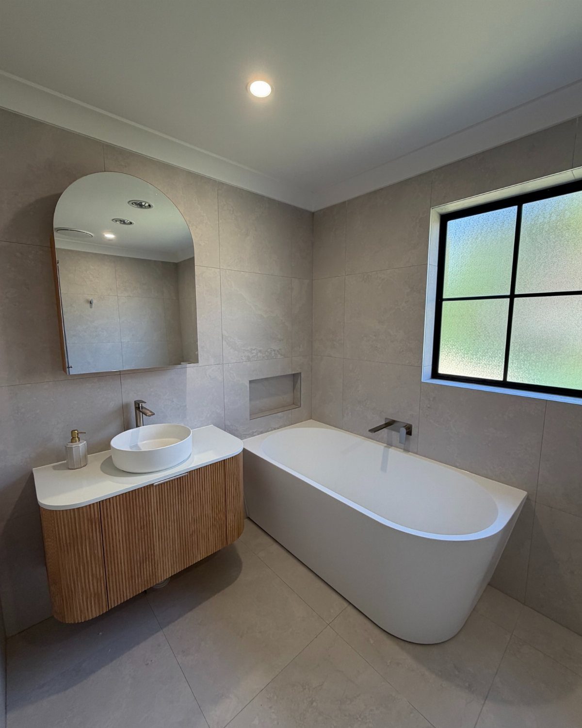 Wall-mounted wooden vanity with white vessel sink next to a white freestanding bathtub.