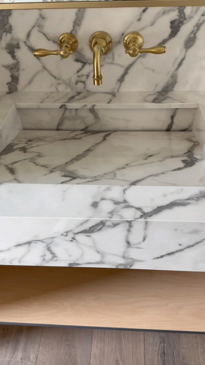 White marble integrated sink and countertop with gold faucets and matching backsplash.