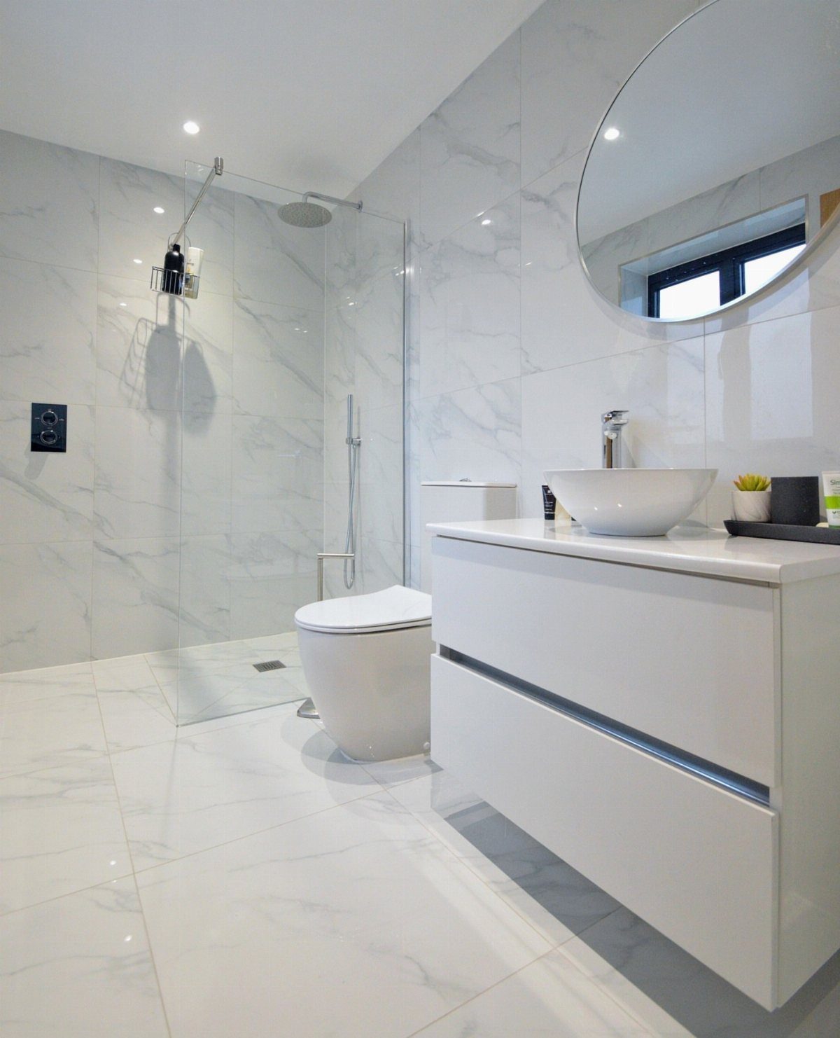 White floating vanity with a vessel sink in a marble tiled bathroom.