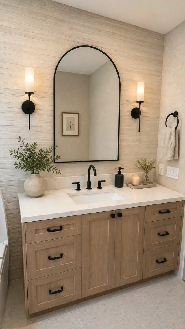 Light wood-grain bathroom vanity with white countertop and arched black-framed mirror.