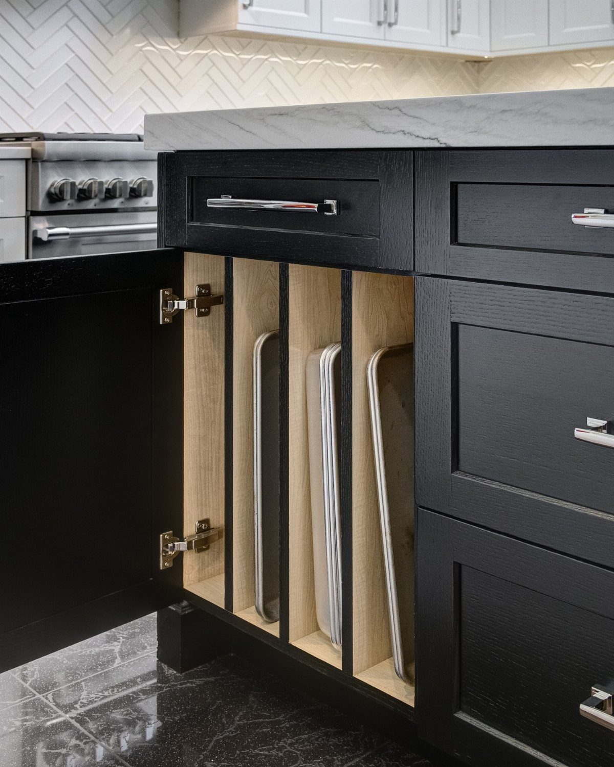 Vertical wooden dividers in a black kitchen cabinet holding white baking sheets.