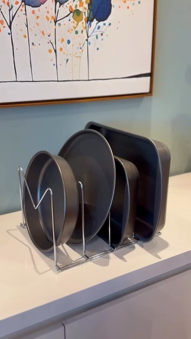 Grey baking pans stored upright in a silver wire magazine rack on a countertop.