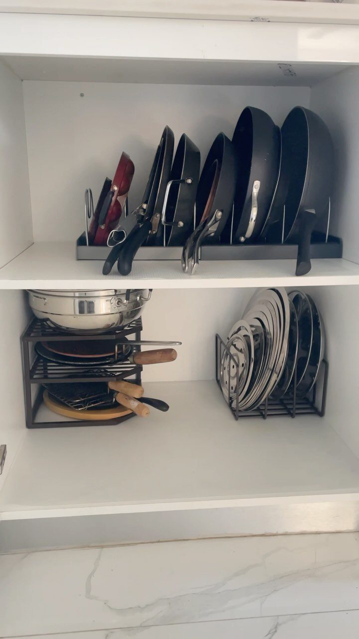 Black frying pans stored vertically in a rack inside a white kitchen cabinet.
