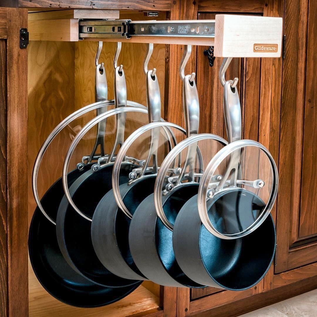Pull-out wooden rack organizing black frying pans and glass lids in a cabinet.