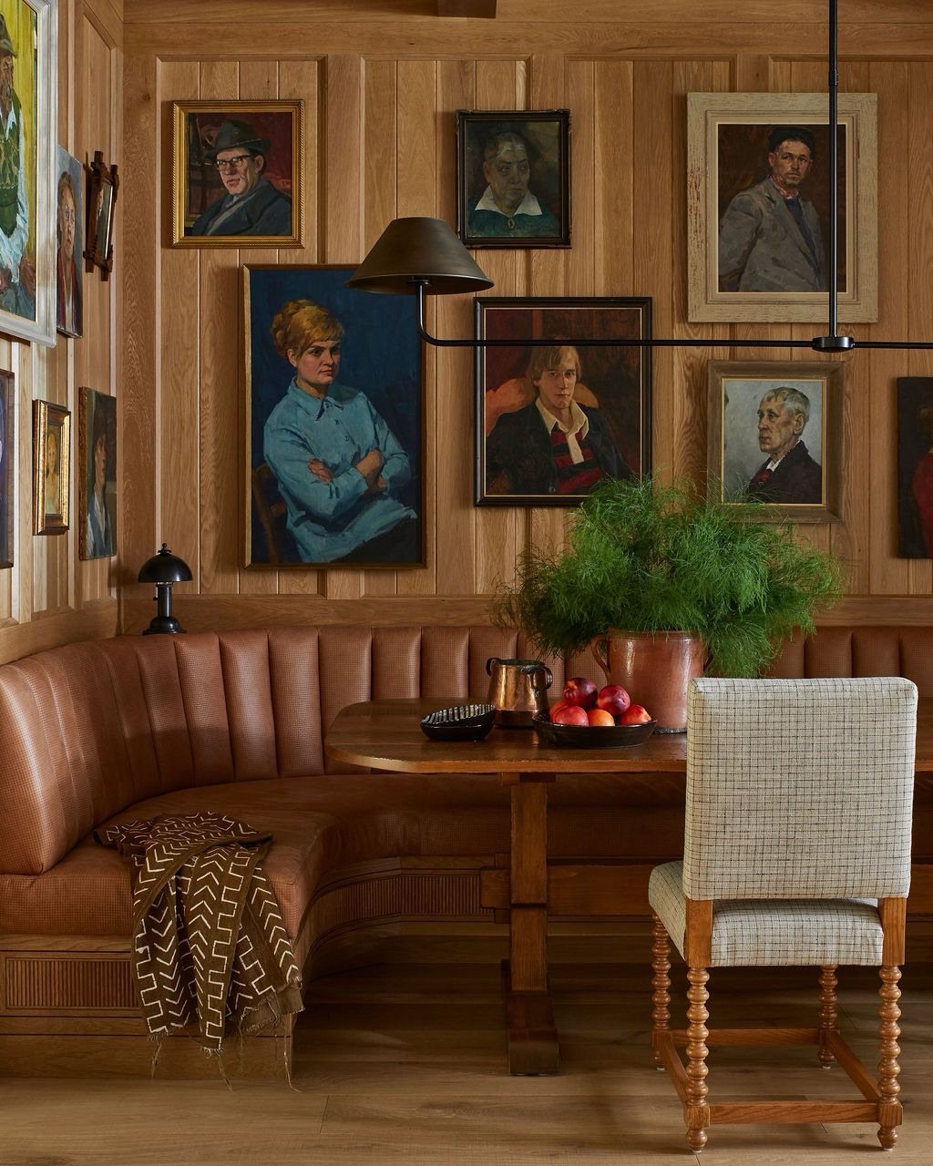 30 Banquette Dining Nook Ideas for Small Kitchens or Corners 20 Brown leather curved banquette and wooden table against brown wood-paneled walls with portraits.