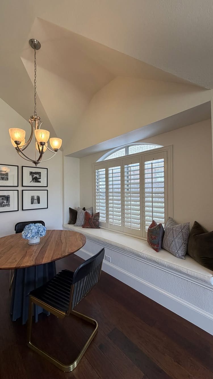 30 Banquette Dining Nook Ideas for Small Kitchens or Corners 22 Long white built-in window seat with pillows next to a round wooden dining table.