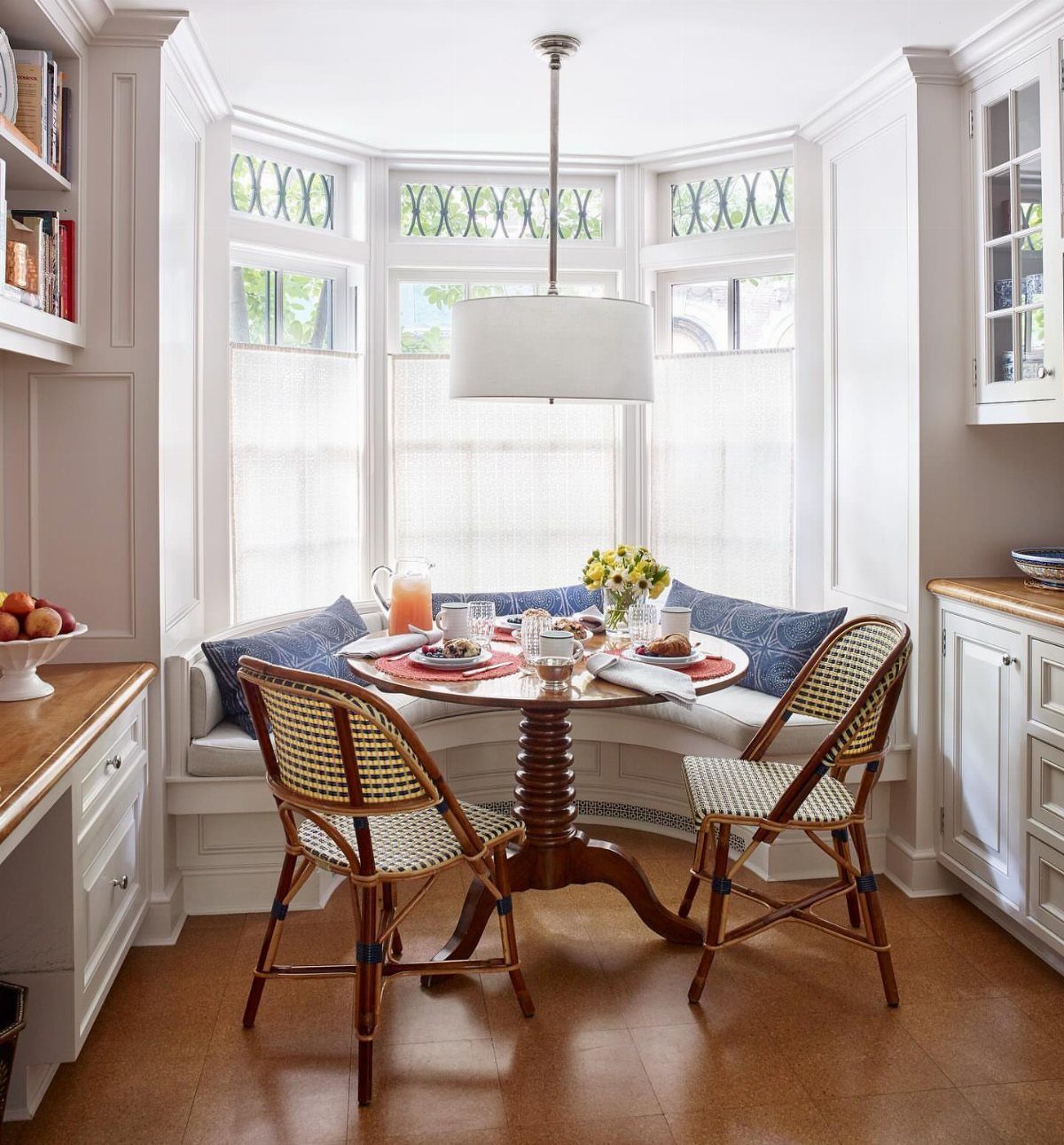 30 Banquette Dining Nook Ideas for Small Kitchens or Corners 5 White built-in banquette following a bay window with a round wooden table and chairs.