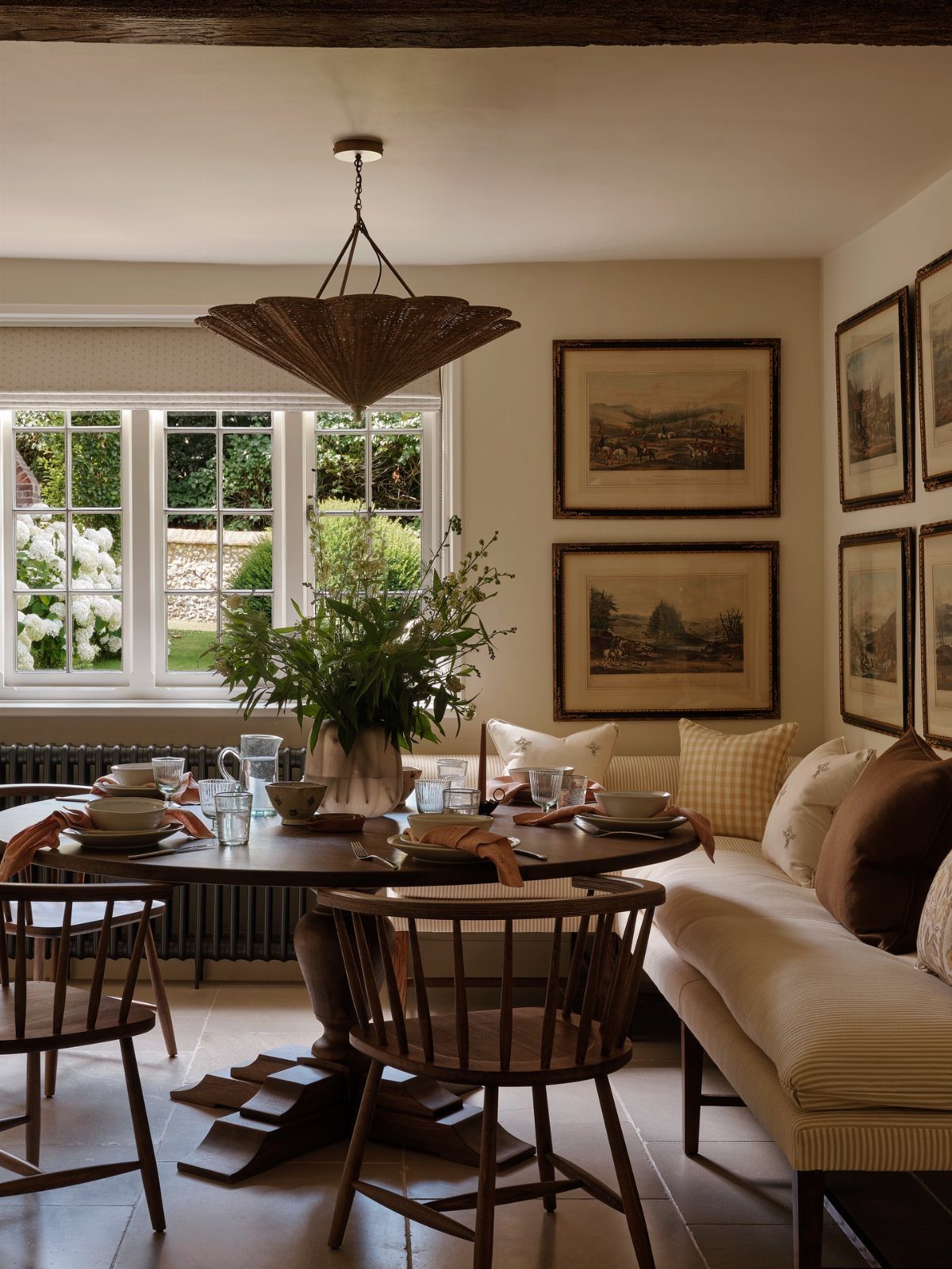 30 Banquette Dining Nook Ideas for Small Kitchens or Corners 19 Cream upholstered freestanding banquette with a round dark wood dining table and chairs.