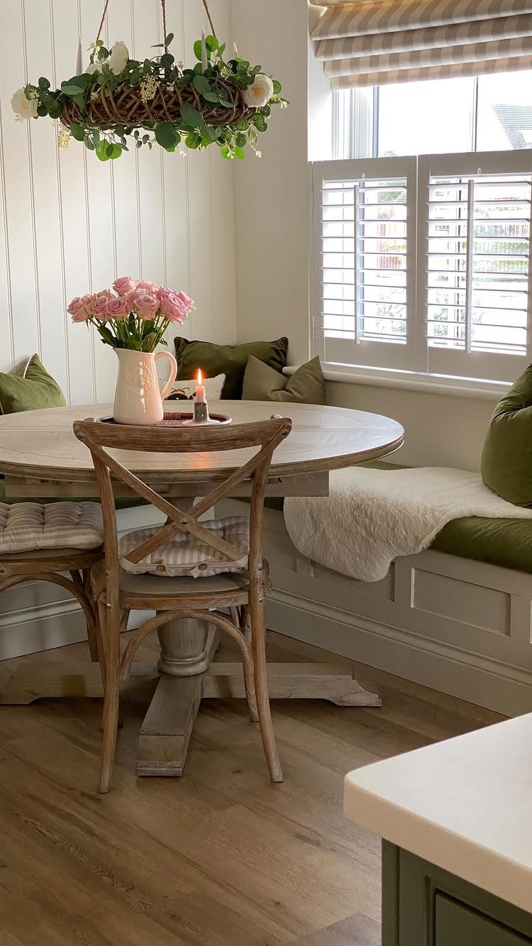 30 Banquette Dining Nook Ideas for Small Kitchens or Corners 10 L-shaped corner banquette with green cushions, round wooden table, and pink roses.
