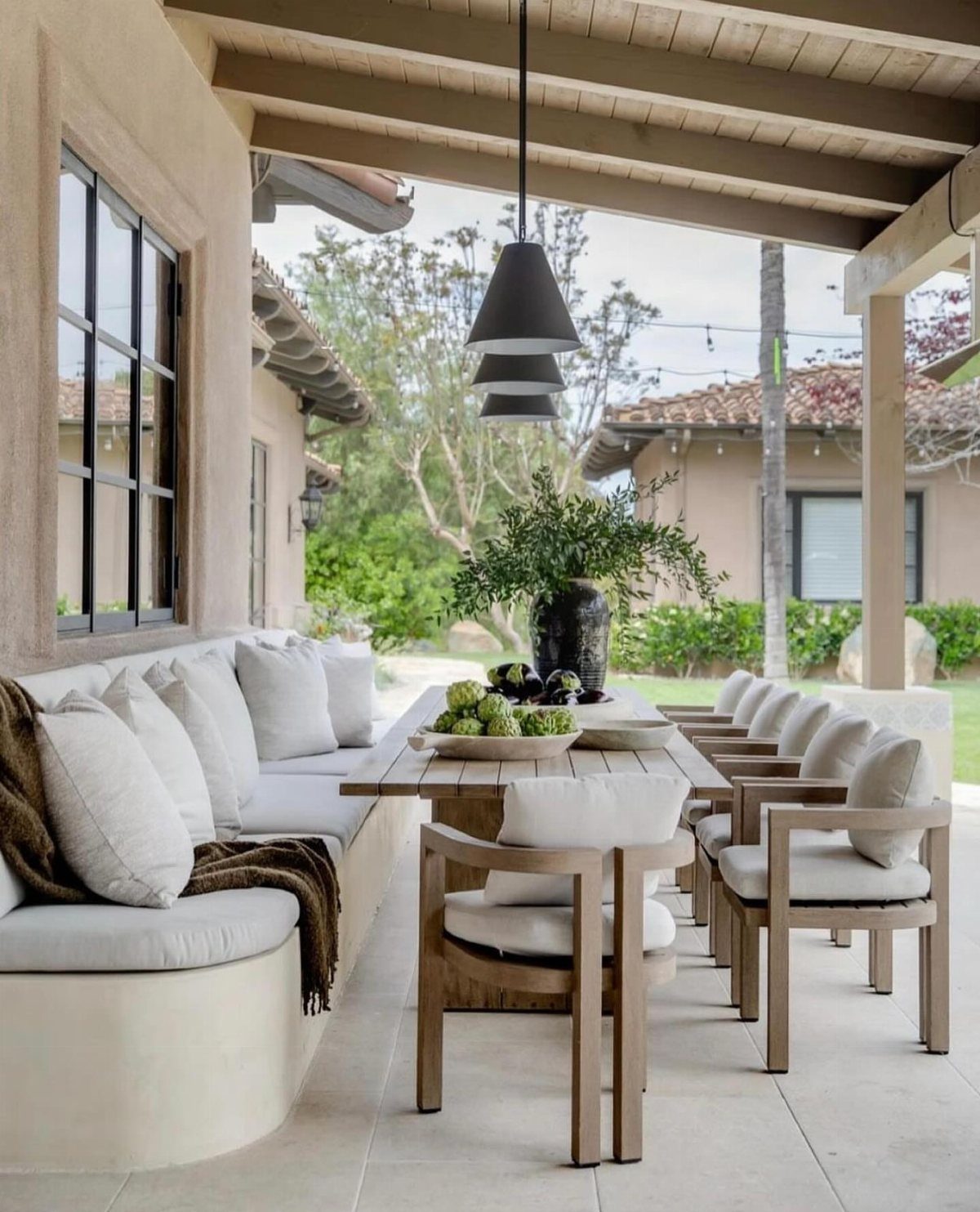 30 Banquette Dining Nook Ideas for Small Kitchens or Corners 16 Curved white built-in banquette seating on a covered outdoor patio with wooden dining furniture.