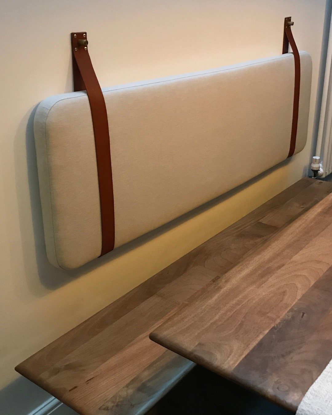 30 Banquette Dining Nook Ideas for Small Kitchens or Corners 2 Beige wall-hung back cushion held by brown leather straps above a wooden table.