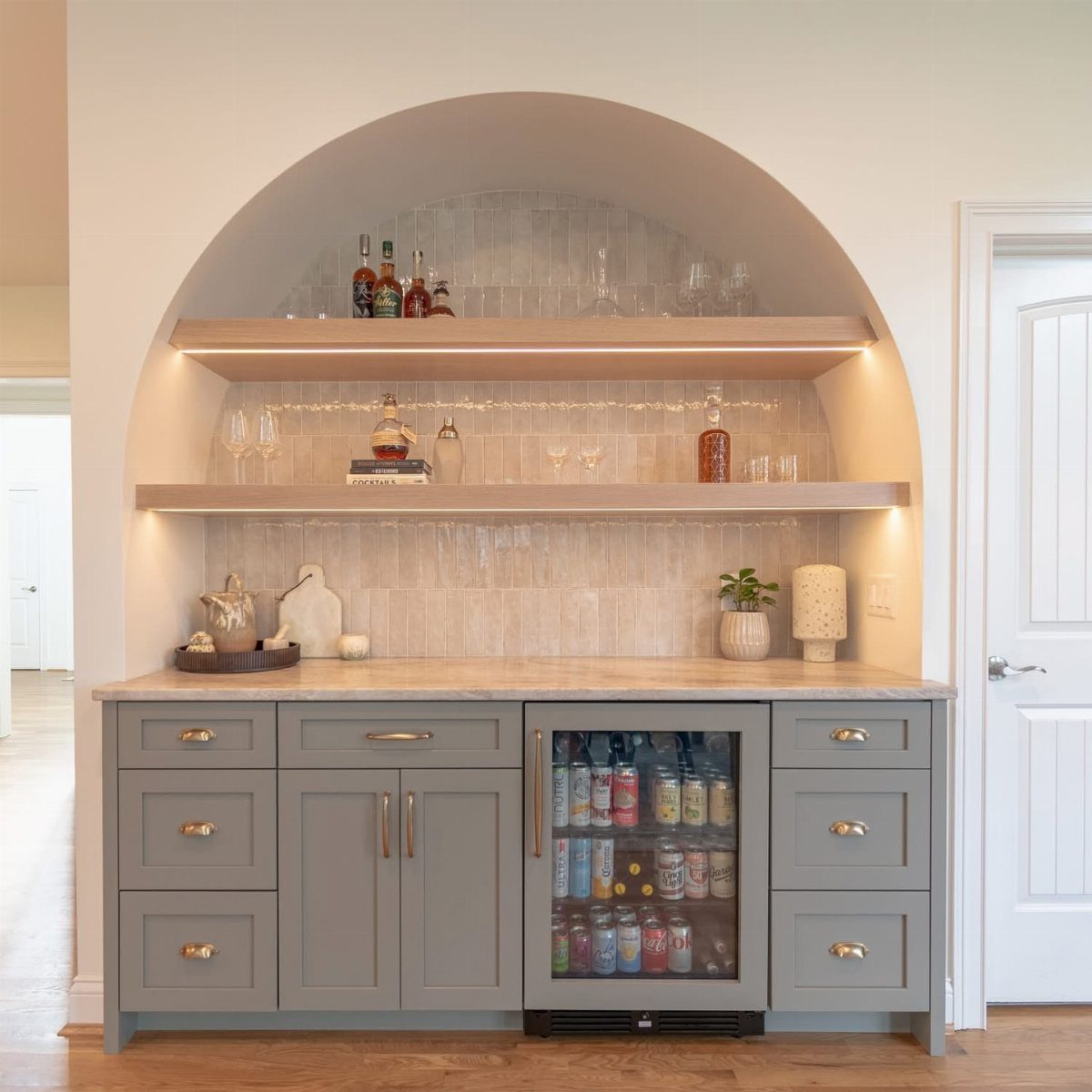Built-in home bar with an arched niche and light marble mosaic tile backsplash.