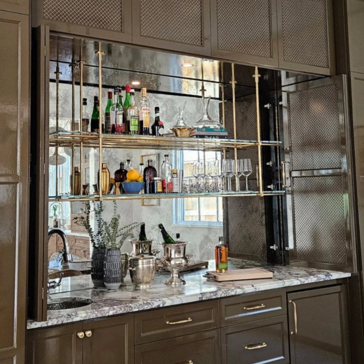Home bar with gold shelving and a mirrored backsplash reflecting liquor bottles.