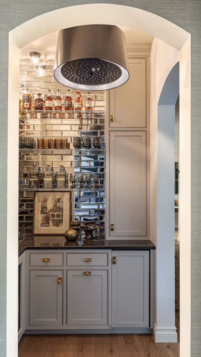 Small home bar with grey cabinets and mirrored backsplash tucked into an arched nook.
