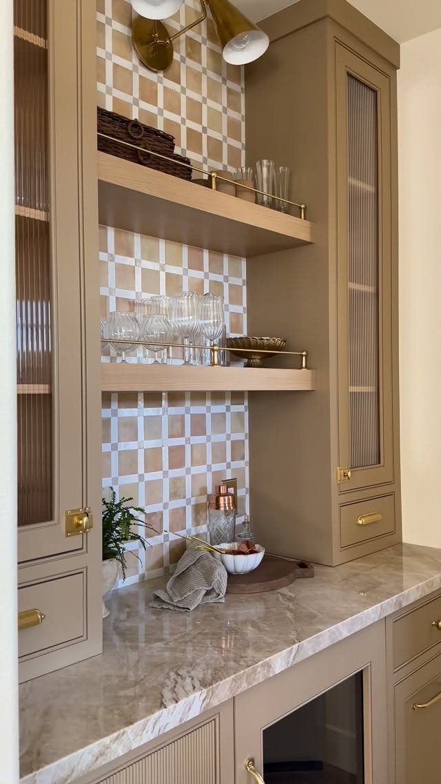 Beige built-in home bar with marble counters, open shelving, and checkered tile backsplash.