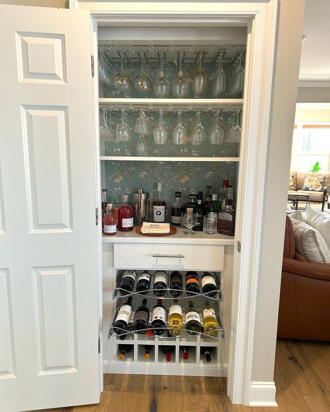 Closet bar with hanging wine glasses, liquor bottles, and a wine rack inside white cabinetry.