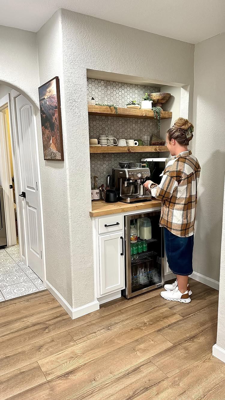 Woman using an espresso machine at a built-in coffee bar with wooden shelves.
