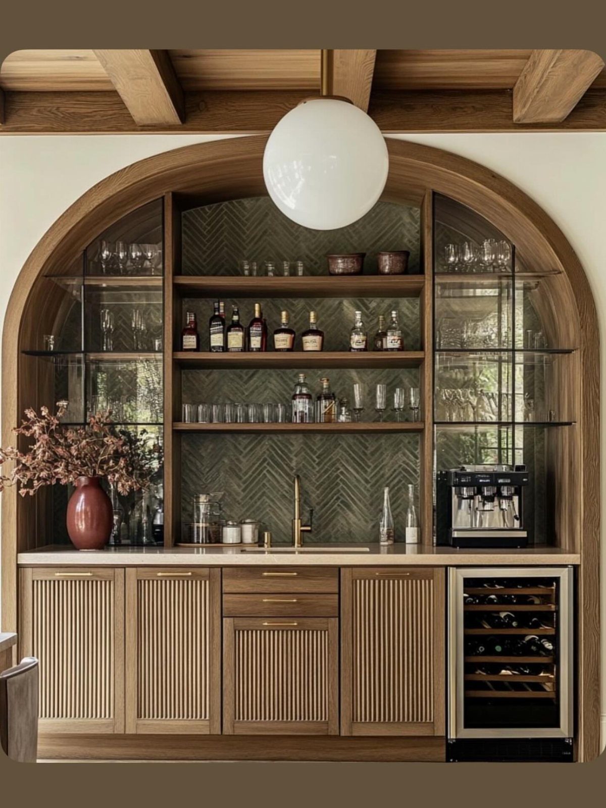 Arched built-in home bar with fluted wood cabinets and green herringbone tile backsplash.