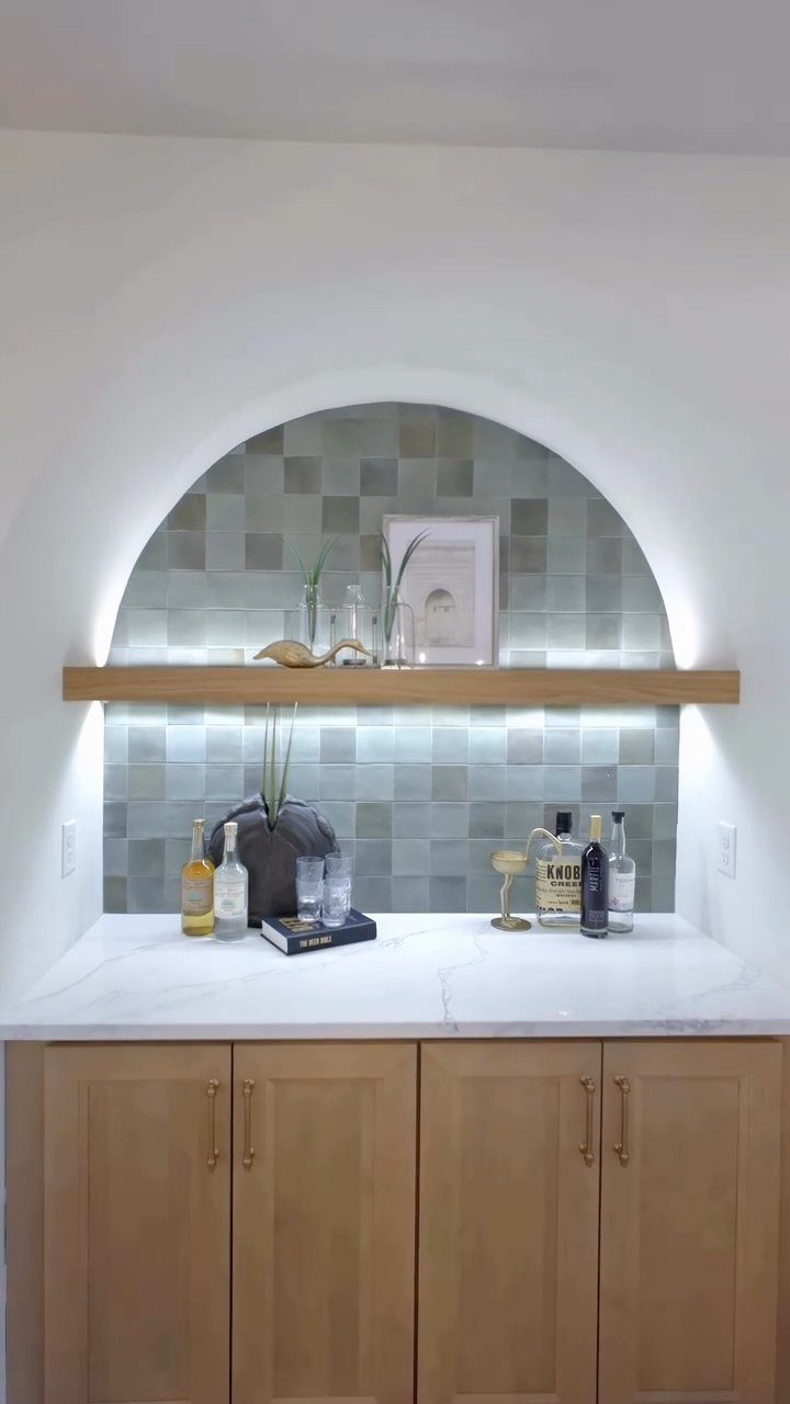 Small dry bar with marble countertop, light wood cabinets, and tiled arched backsplash.
