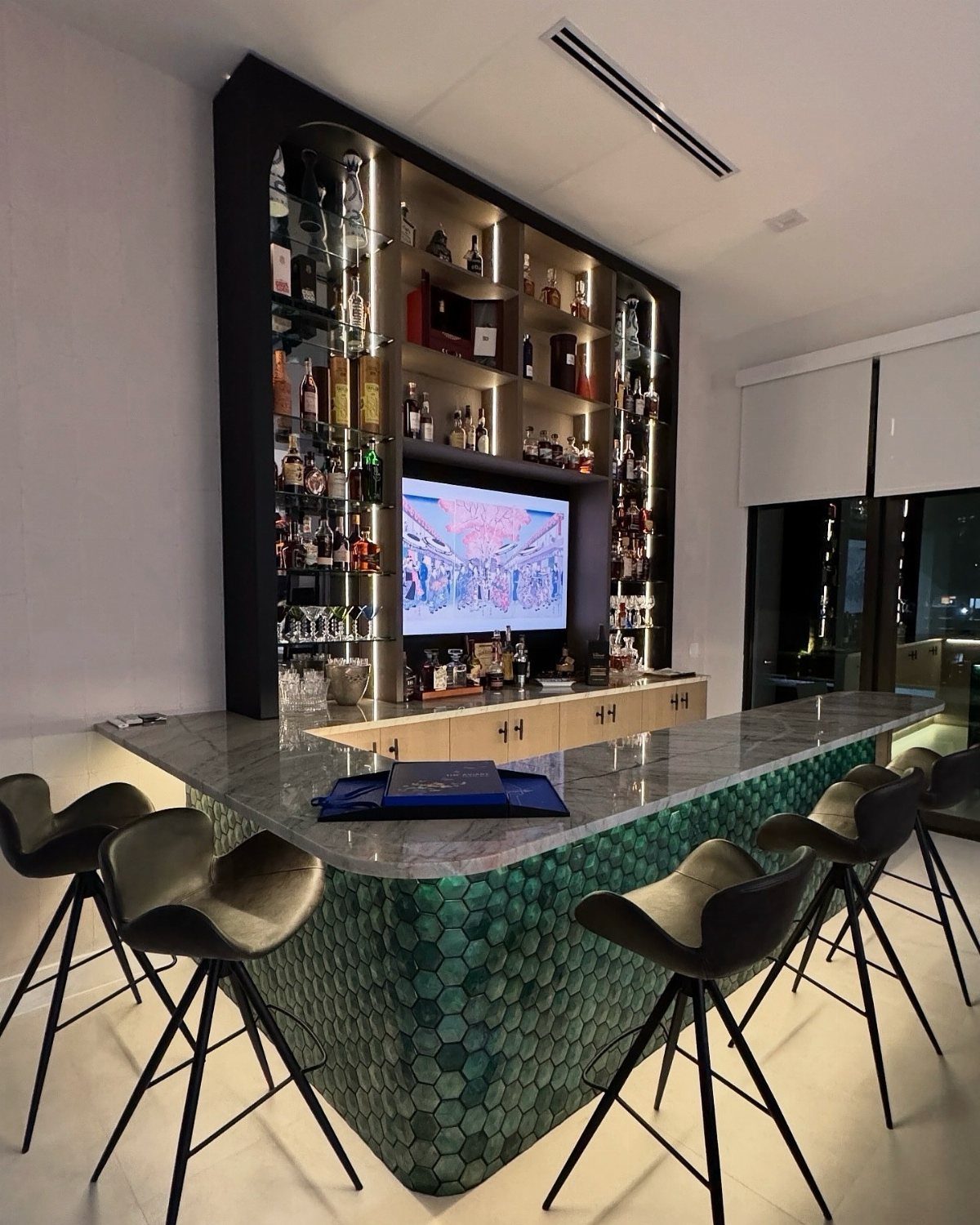 Modern home bar with green hexagonal tiles, marble countertop, and built-in liquor shelves.