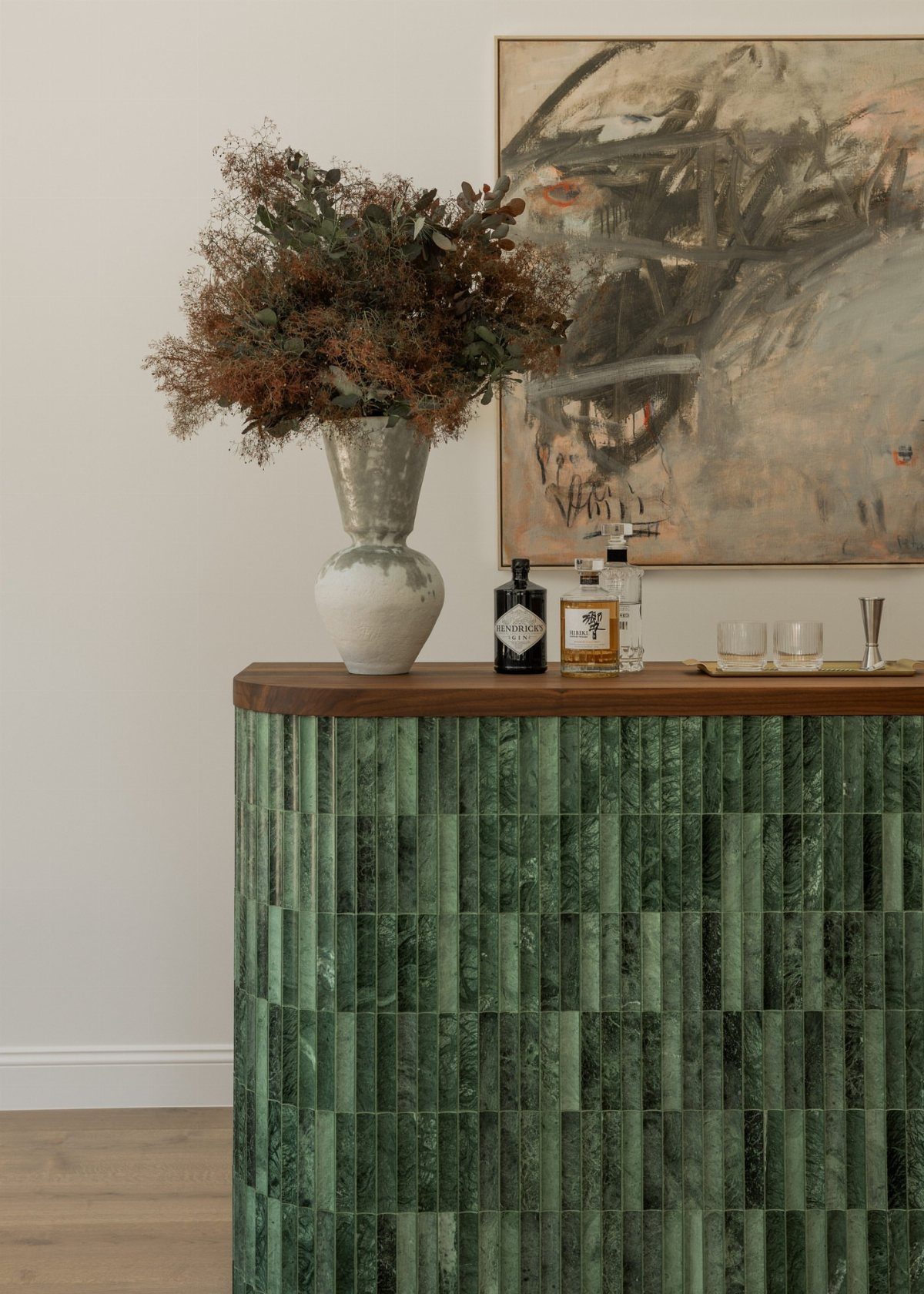 Green marble tiled home bar with a wooden top and dried flower arrangement.