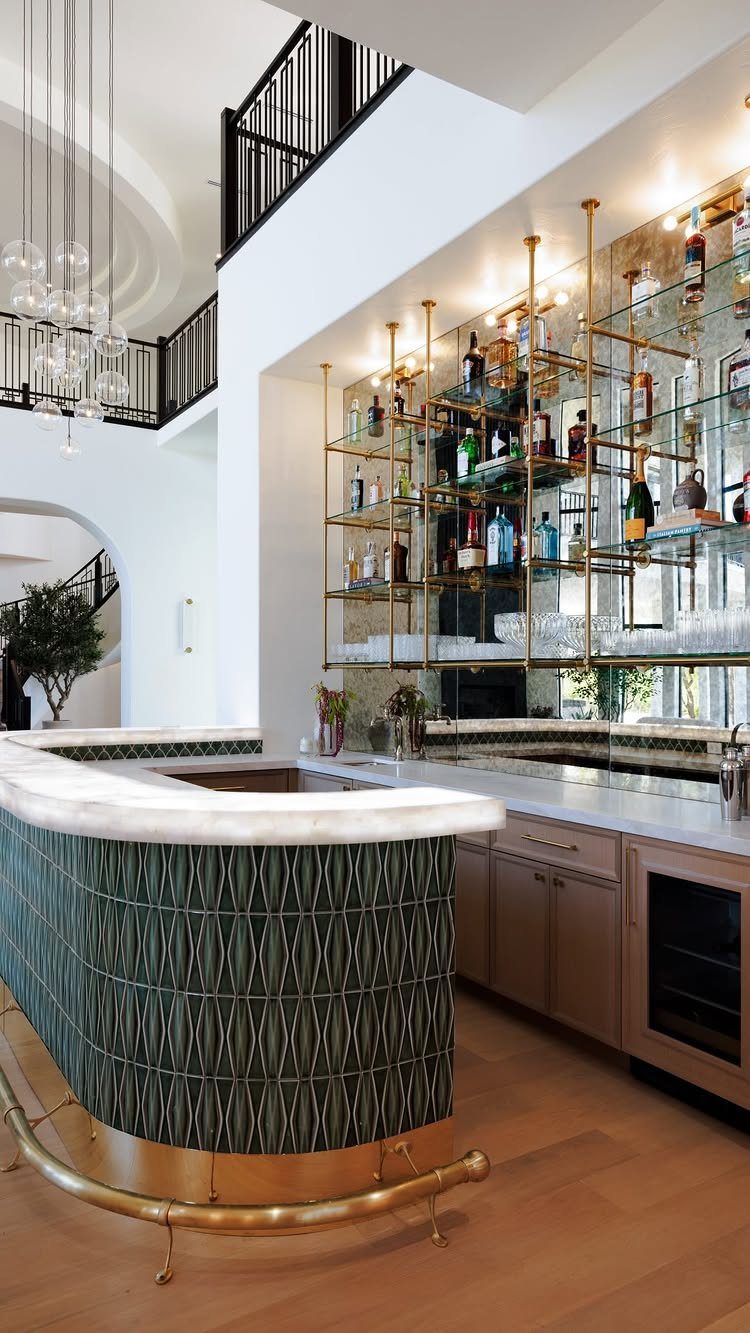 Curved home bar with green patterned tiles, gold trim, and mirrored bottle shelves.