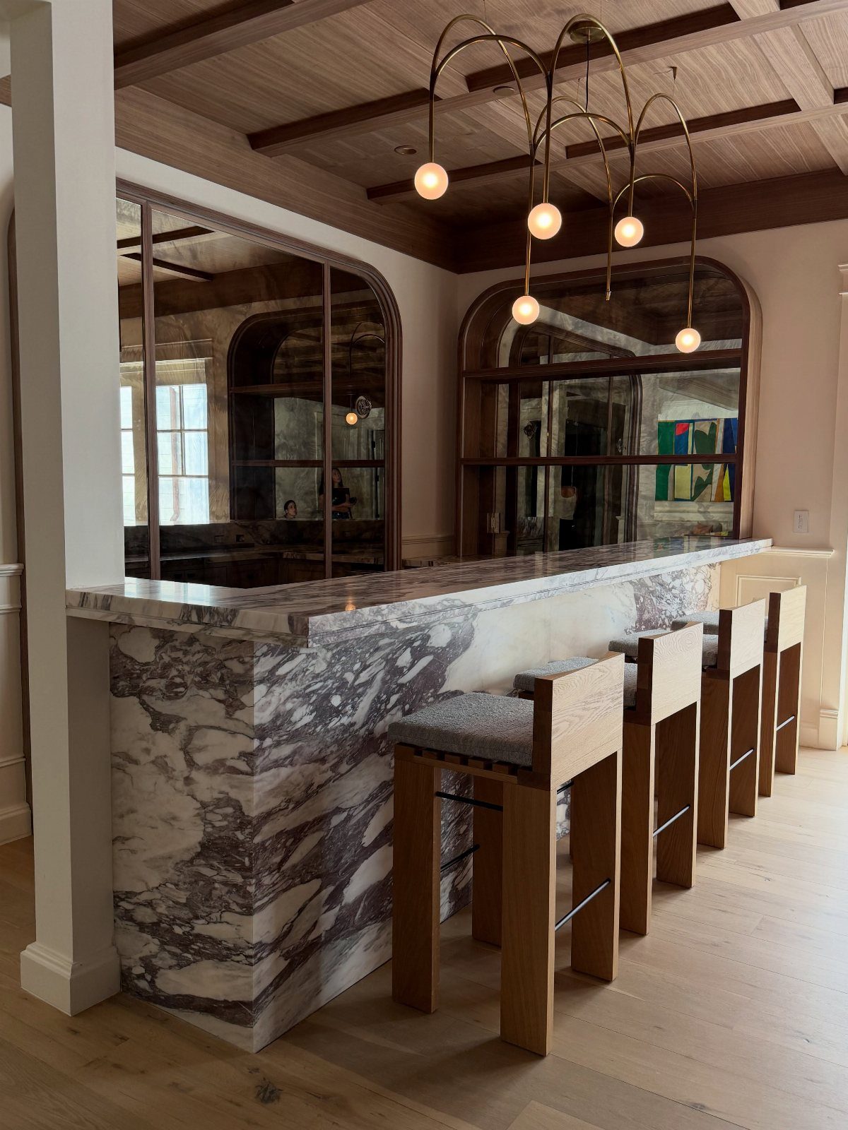 Marble home bar with arched mirrors and gold chandelier lighting in a room.