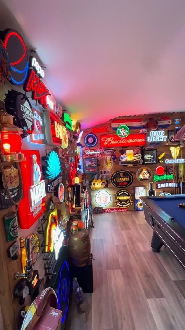 Game room with neon beer signs on wood walls and a pool table.
