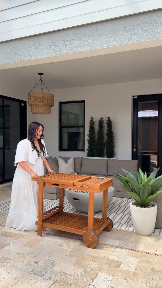 Wooden bar cart on wheels on a paved patio with a woman standing beside it.