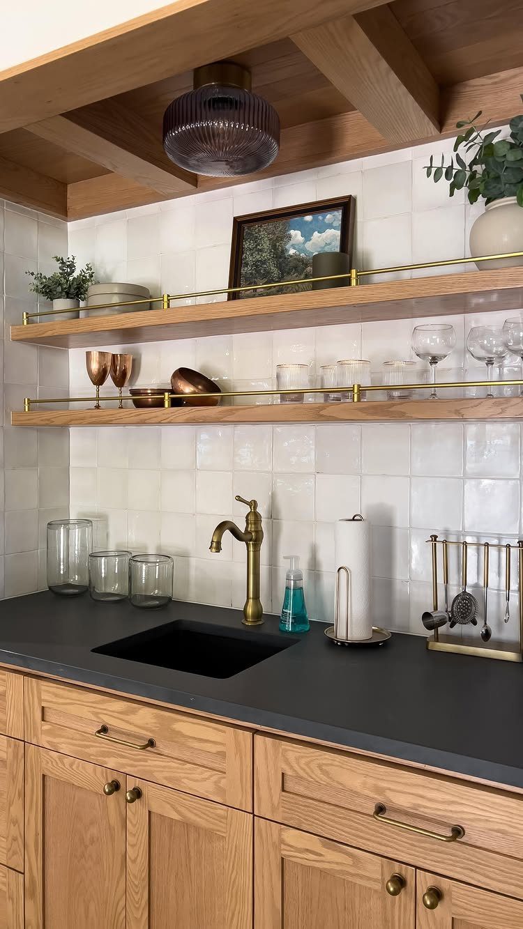Home wet bar with dark countertops, gold faucet, and white tile backsplash.